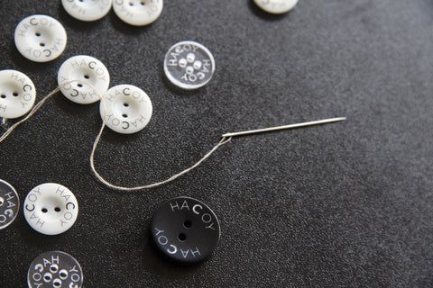 HACOY buttons with a needle and thread on a dark cloth
